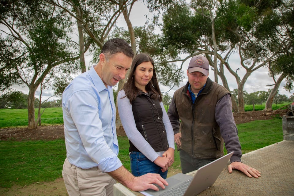 An adviser and two farmers looking at a laptop outdoors