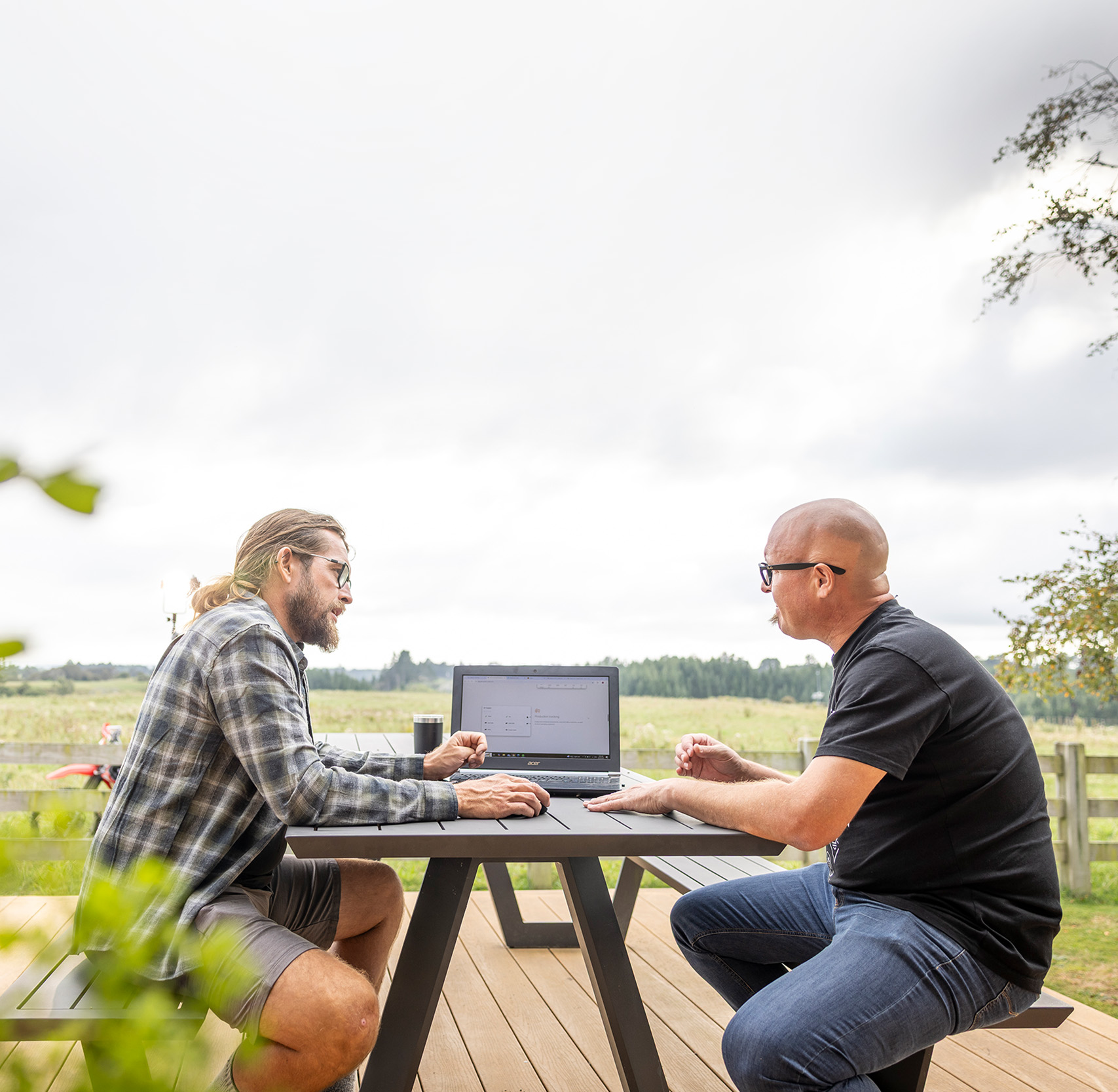 A farmer and his adviser working through farm numbers on a laptop at an outdoor table