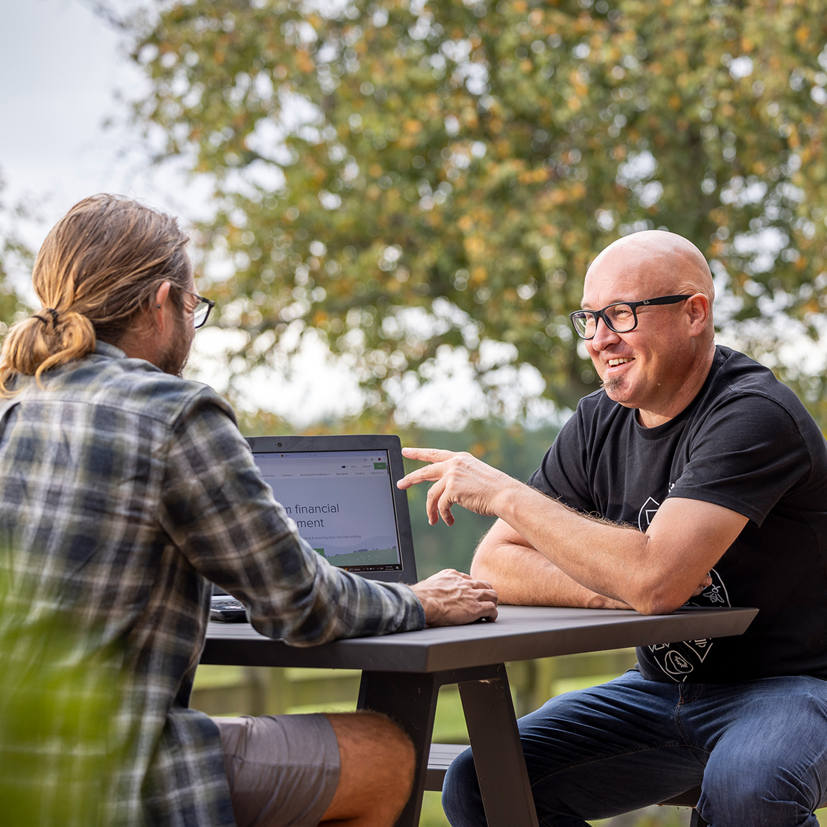 An adviser pointing something out on screen to a farmer across an outdoor table